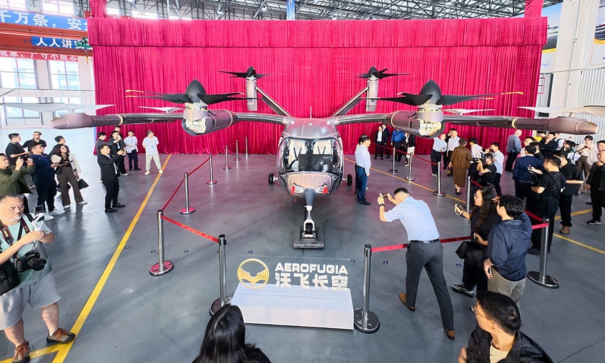 Guests take photos of the first AE200-100 large passenger eVTOL (electric vertical takeoff and landing aircraft) for low-altitude travel after it rolls off the production line in Chengdu, Southwest China's Sichuan Province, on September 29, 2025. The milestone marks the completion of major body section assembly and the installation of core onboard systems, moving the model into the airworthiness certification sprint and pre-production phase. Photo: VCG