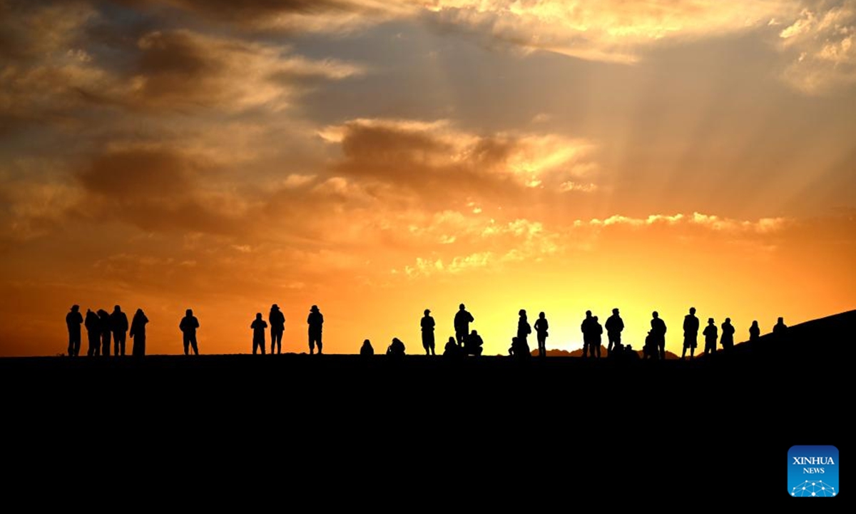 Tourists enjoy the sunrise over the desert at the Mingsha Mountain and Crescent Spring scenic area in Dunhuang City, northwest China's Gansu Province, Oct. 2, 2025. With China's Mid-Autumn Festival falling alongside National Day this year, people spend their leisure time through various ways during the eight-day holiday. (Photo by Zhang Xiaoliang/Xinhua)

