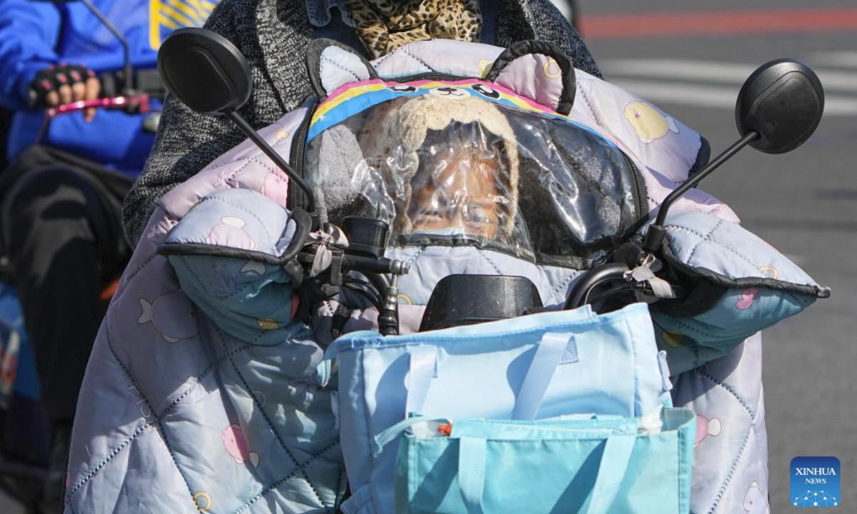 A child hides from the wind behind a windshield cover on a motorcycle in Beijing, capital of China, Oct. 18, 2025. Affected by strong cold air, Beijing is hit by a cold wave. (Xinhua/Ju Huanzong)