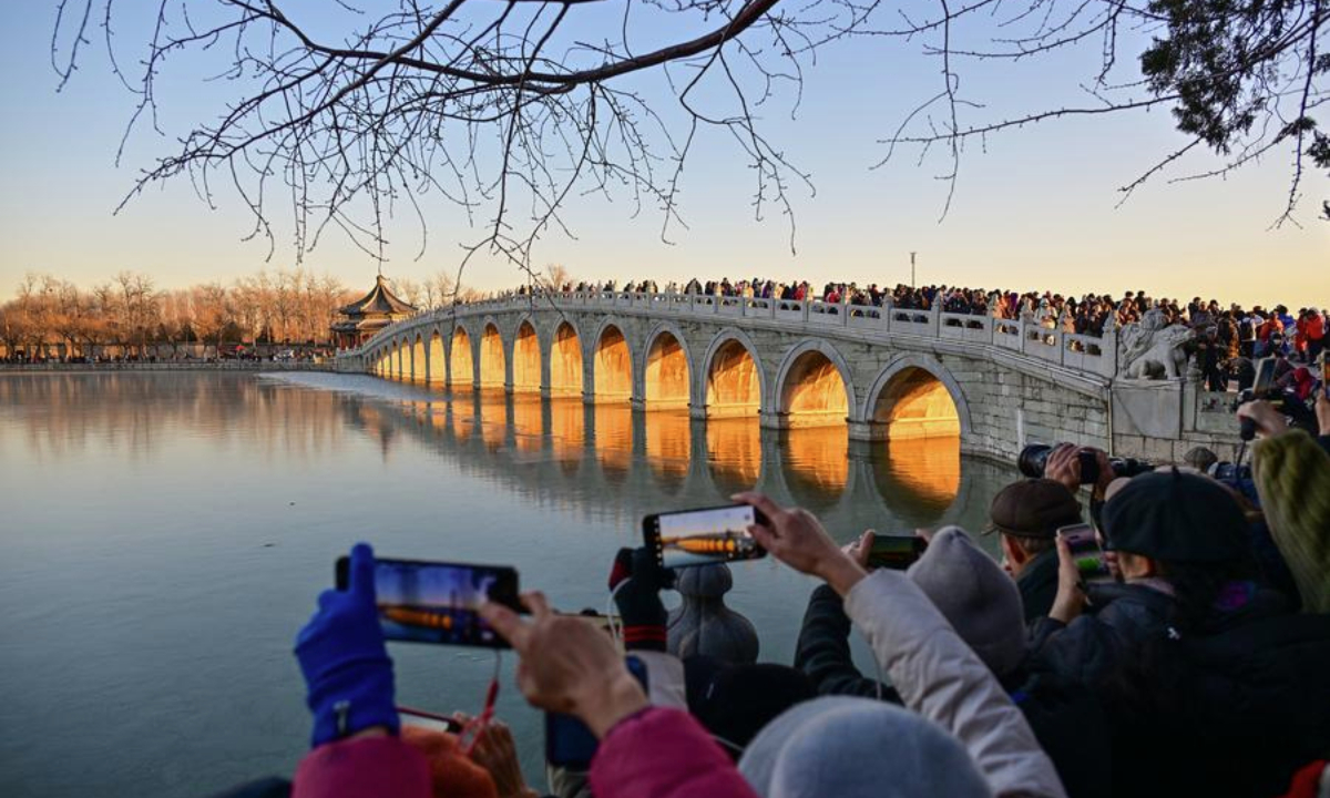 Visitors take photos of the illuminated 17-Arch Bridge at sunset in the Summer Palace in Beijing, capital of China on Dec. 22, 2024. (Xinhua/Li Xin)