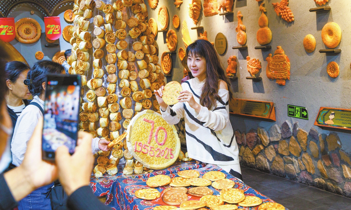 Amid the Xinjiang Uygur Autonomous Region's 70th founding anniversary, a visitor at the Xinjiang International Grand Bazaar in Urumqi on September 23, 2025, poses for photos holding naan, a traditional local delicacy. Photo: IC