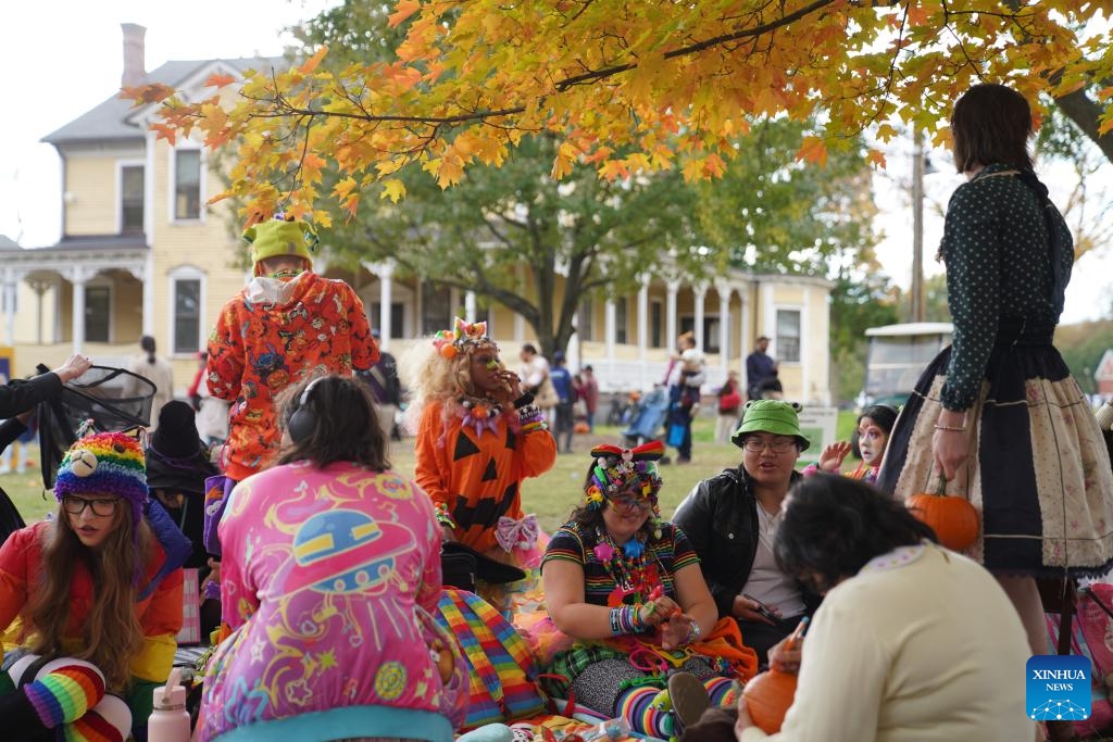 People gather under a tree during a fall festival at the Governors Island in New York, the United States, on Oct. 25, 2025. A festival was held at the Governors Island in New York on Saturday, attracting locals and visitors to celebrate the fall harvest with various family-friendly activities.  (Photo: Xinhua)