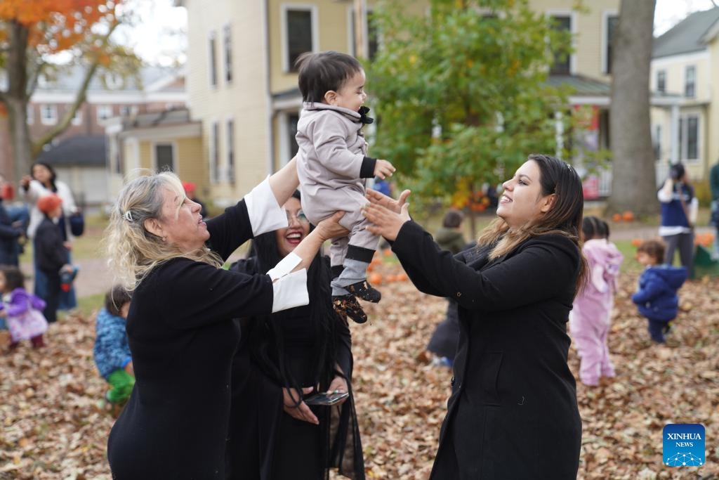 People hold a baby during a fall festival at the Governors Island in New York, the United States, on Oct. 25, 2025. A festival was held at the Governors Island in New York on Saturday, attracting locals and visitors to celebrate the fall harvest with various family-friendly activities.  (Photo: Xinhua)