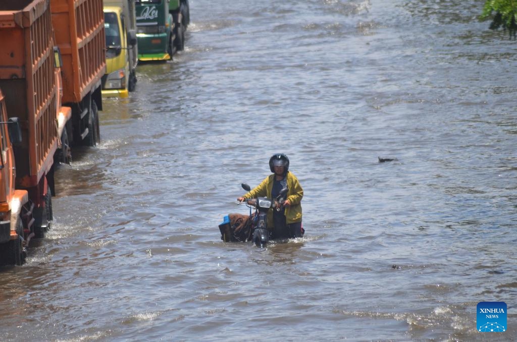 A woman wades through flood waters with her motorbike after heavy rain hit Semarang, Central Java, Indonesia, Oct. 25, 2025. (Photo: Xinhua)