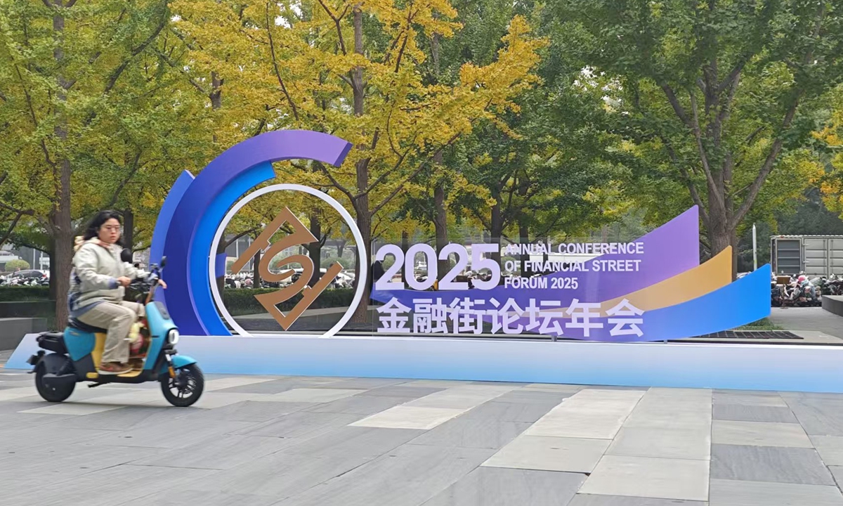 A person rides an electric bike past a display board featuring the logo of the ongoing Annual Conference of Financial Street Forum 2025 in Beijing's Xicheng district on October 29, 2025. Photo: Yin Yeping/GT
