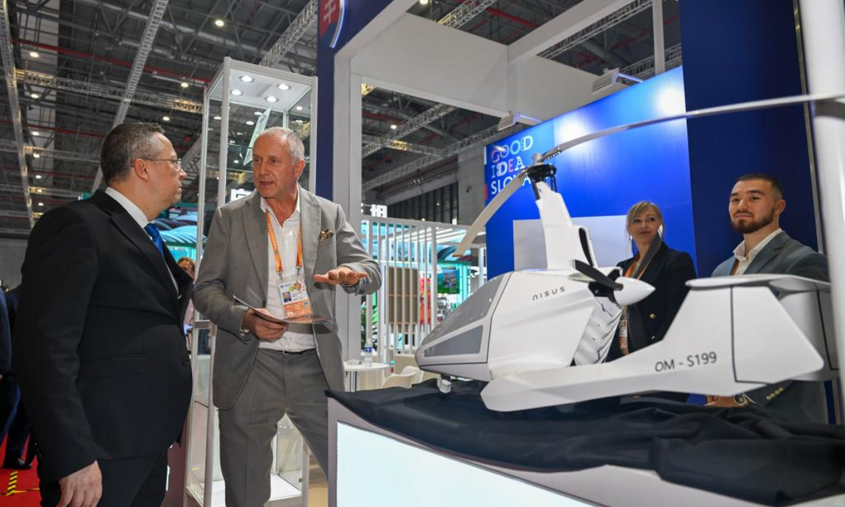An exhibitor (2nd L) introduces an aircraft product to a visitor (1st L) at the Slovakia Pavilion of the eighth China International Import Expo (CIIE) in east China's Shanghai, Nov. 5, 2025. (Xinhua/Chen Haoming)