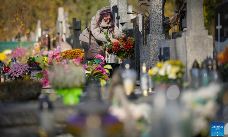 A woman arranges flowers on a grave to commemorate All Saints' Day at a cemetery in Warsaw, Poland on Nov. 1, 2025. Saturday marks All Saints' Day in Poland, when people traditionally return home to reunite with family members and visit cemeteries to honor their ancestors. (Photo: Xinhua)