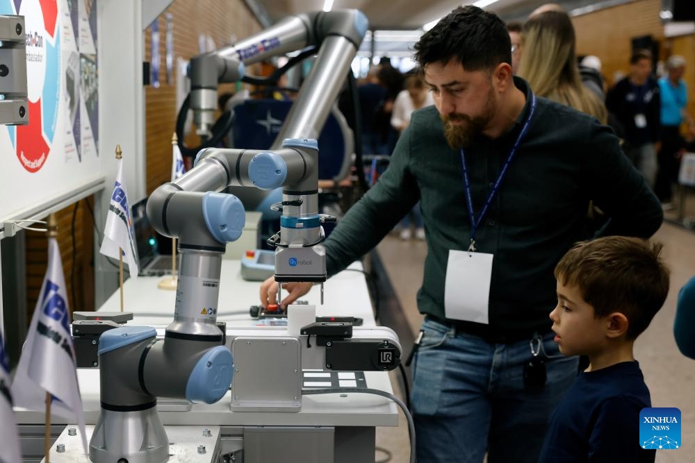 A boy listens to a participant introducing a robot during the 4th edition of the Robofest, a technology festival, at the Politehnica University of Bucharest in Bucharest, Romania, Nov. 1, 2025. The three-day festival including the 16th edition of the Robochallenge is held here from Oct. 31 to Nov. 2. (Photo: Xinhua)