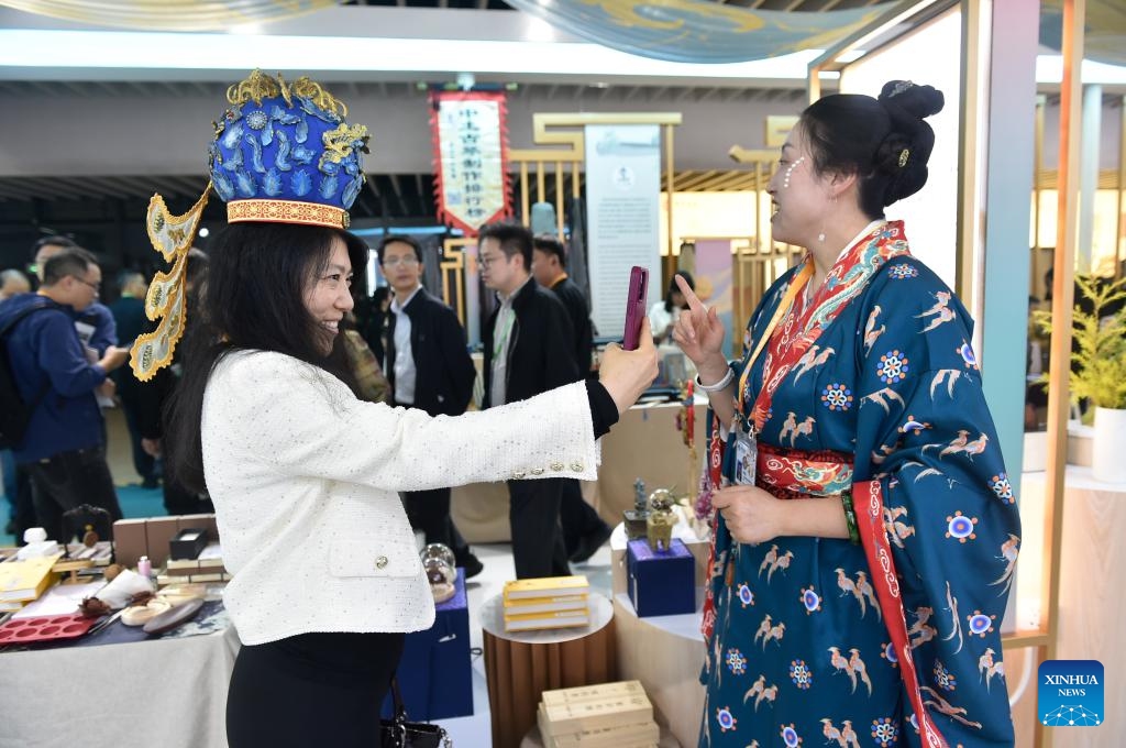 A visitor (L) tries on a crown at the booth of China's Hubei Province during the eighth China International Import Expo (CIIE) in east China's Shanghai, Nov. 6, 2025. The CIIE is not only a global platform for the trade of goods and services but also a grand event for the exchange of cultures and ideas between China and the world. (Xinhua/Lu Peng)