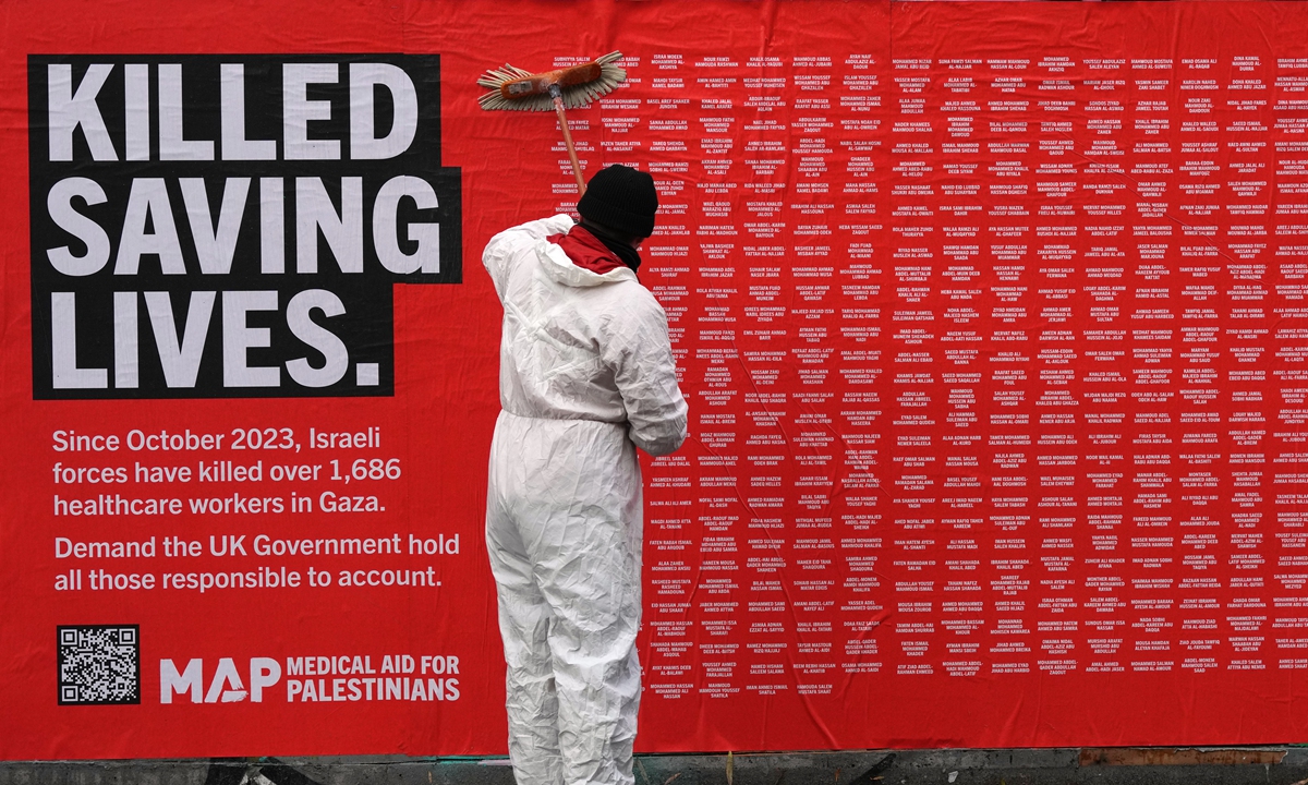 A worker puts up a poster with names of killed aid workers on a wall as Medical Aid for Palestinians unveils a public memorial wall in London, the UK, on November 25, 2025, to honor the Palestinian healthcare workers killed. Photo: VCG