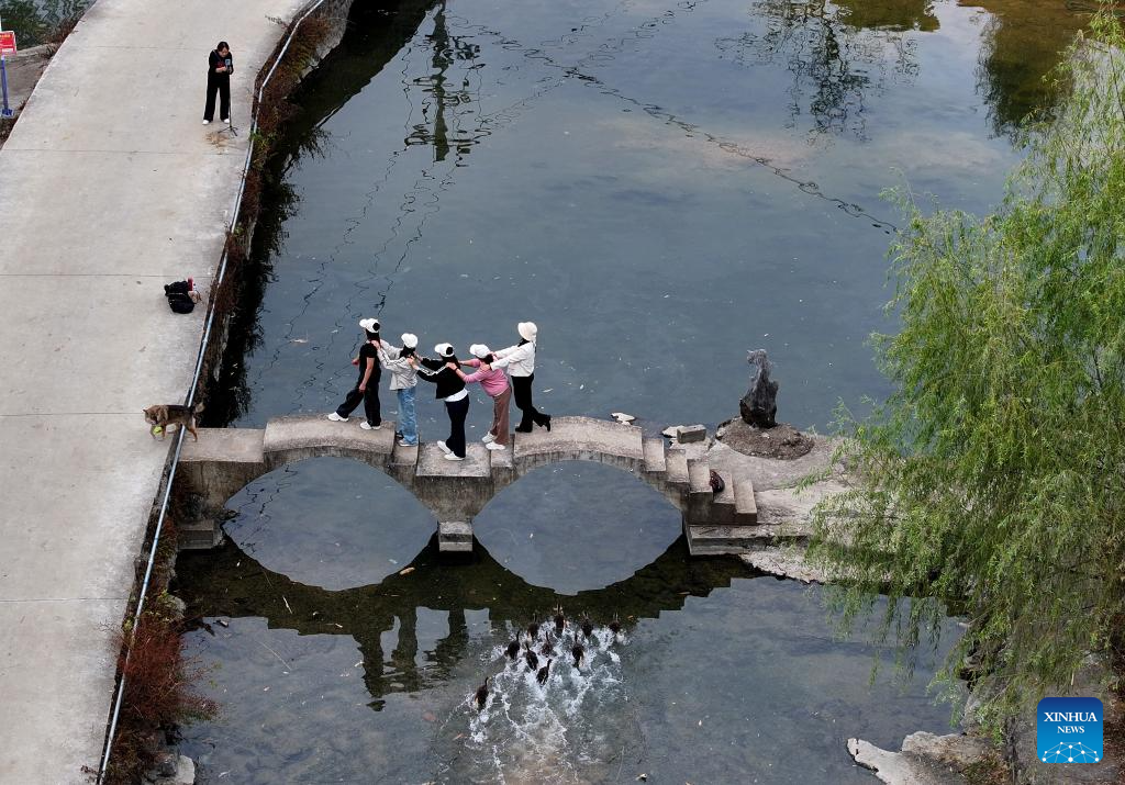 An aerial drone photo taken on Nov. 1, 2025 shows tourists posing for photos on a small bridge in a village of Jinde Town in Liuzhou City, south China's Guangxi Zhuang Autonomous Region. Mountains, gullies and streams surrounding the villages across Guangxi's rural area make bridges the must for production and daily life. Small bridges are not only important transportation link, but also play a crucial role in culture inheritance, industrial development and rural revitalization. (Xinhua/Huang Xiaobang)