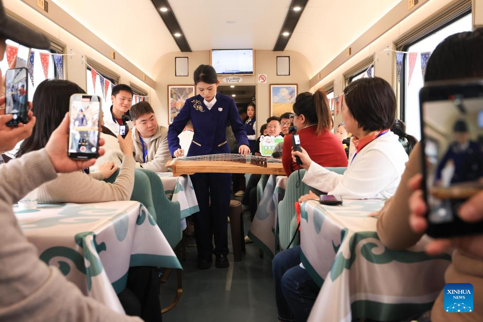 A staff member plays Guzheng, a traditional Chinese musical instrument, for passengers onboard the Train Y783 on Nov. 26, 2025. Train Y783, an ice-and-snow themed tourism train, was launched at Harbin Railway Station and started a six-day trip on Wednesday. The train showcases the charm of northeastern China through themed decorations, tour guide services and interactive activities, in an effort to promote winter tourism and inject new vitality into ice and snow economy. (Photo by Xu Shuai/Xinhua)