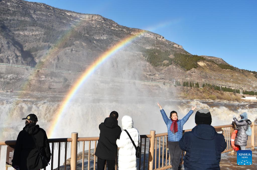 Tourists take photos with a double rainbow over the Hukou Waterfall in the background in Jixian County, north China's Shanxi Province, Dec. 3, 2025. (Photo by Lyu Guiming/Xinhua)