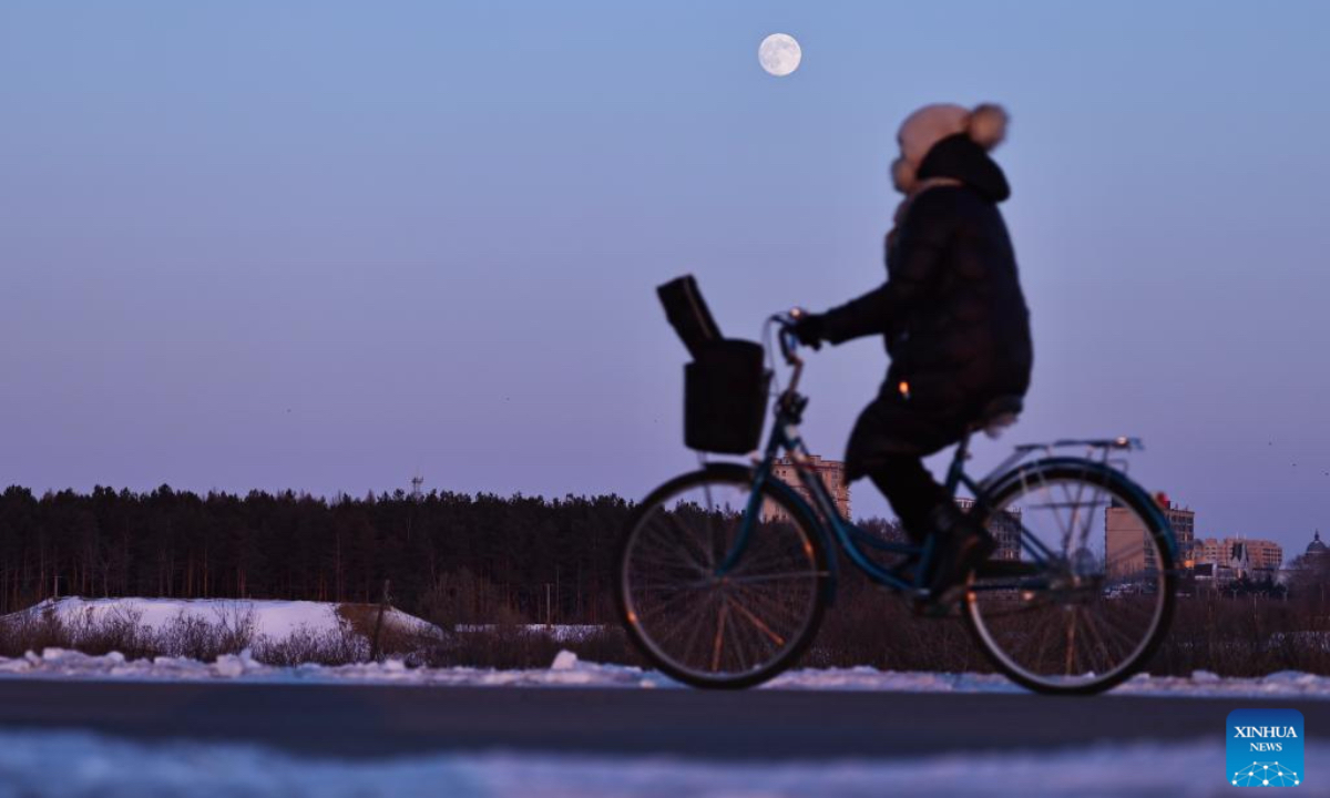 A citizen cycles as a full moon is seen over Tongjiang City, northeast China's Heilongjiang Province, Dec. 4, 2025. This year's second-largest full moon to the eyes of lunar observers will appear on Friday morning, but the best viewing time falls on Thursday evening. (Photo by Liu Wanping/Xinhua)