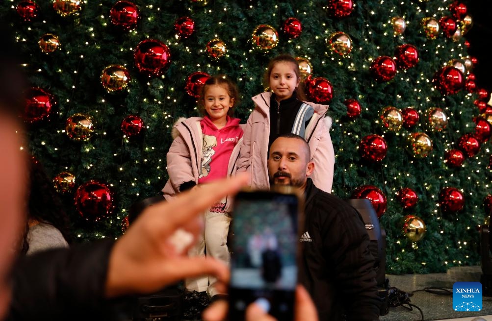 People take photos in front of a Christmas tree at the Manger Square in Bethlehem, southern West Bank on Dec. 6, 2025. Hundreds of residents and visitors attended a Christmas tree-lighting event here Saturday to mark the beginning of this year's Christmas celebrations. (Photo by Mamoun Wazwaz/Xinhua)