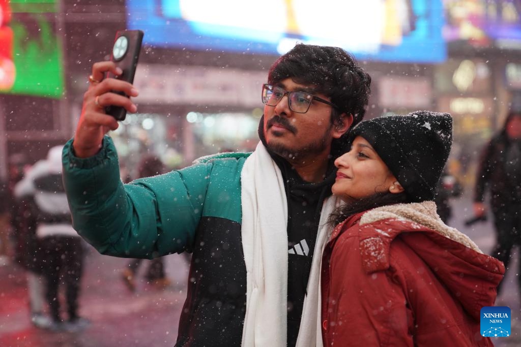 A couple takes a selfie in snow at Times Square in New York, the United States, on Dec. 14, 2025. (Xinhua/Zhang Fengguo)