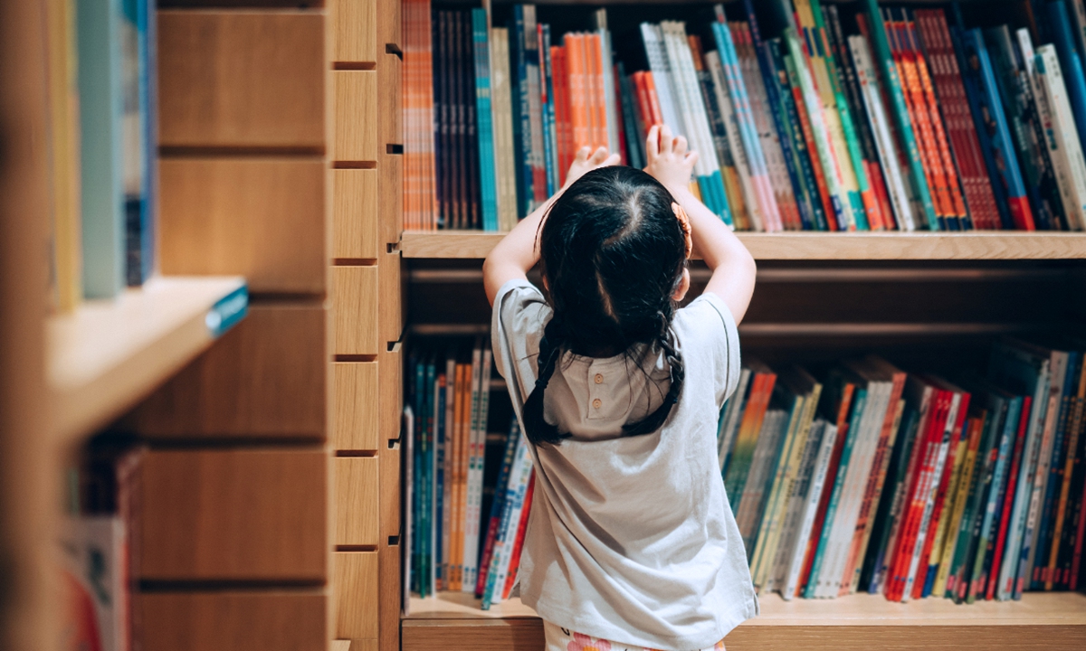 A girl selects book from a bookshelf. Photo: VCG