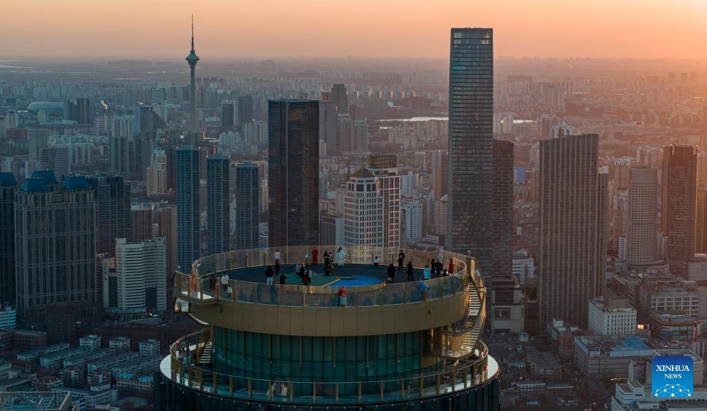 An aerial drone photo taken on Dec. 20, 2025 shows visitors enjoying the night urban view at the Jinwan Yunding sightseeing deck in Heping District of Tianjin, north China. Recently, the Jinwan Yunding sightseeing deck, located at the Jinwan Plaza in Heping District of Tianjin, has begun operation. Visitors can ascend to the 300-meter-high rooftop to overlook Tianjin's urban view. (Xinhua)