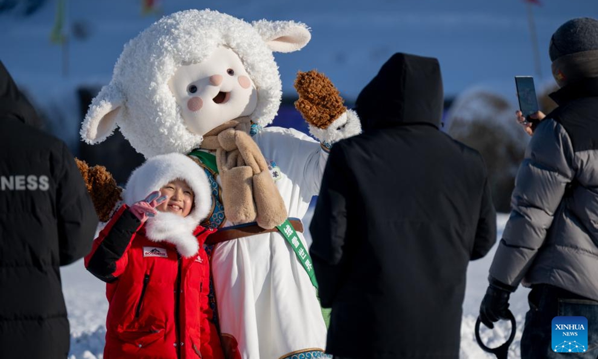 A child poses for photos with a cartoon character during the opening ceremony of the 21st Ice and Snow Nadam Fair of the Inner Mongolia Autonomous Region in Hailar District of Hulun Buir, north China's Inner Mongolia Autonomous Region, Dec. 21, 2025. The nadam fair kicked off here on Sunday, attracting tourists from home and abroad. (Xinhua/Lian Zhen)