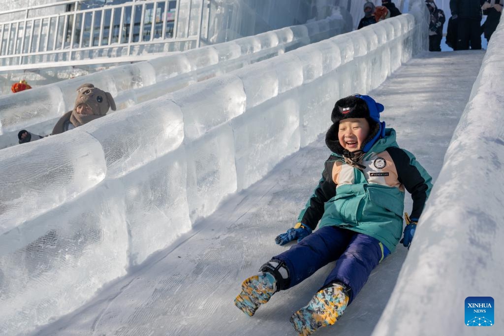 A child enjoys playing on an ice-made slide during the opening ceremony of the 21st Ice and Snow Nadam Fair of the Inner Mongolia Autonomous Region in Hailar District of Hulun Buir, north China's Inner Mongolia Autonomous Region, Dec. 21, 2025. The nadam fair kicked off here on Sunday, attracting tourists from home and abroad. (Xinhua/Lian Zhen)