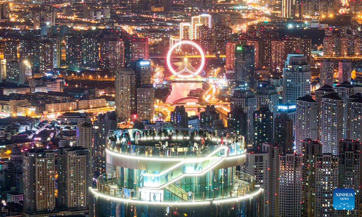 An aerial drone photo taken on Dec. 20, 2025 shows visitors enjoying the night urban view at the Jinwan Yunding sightseeing deck in Heping District of Tianjin, north China. Recently, the Jinwan Yunding sightseeing deck, located at the Jinwan Plaza in Heping District of Tianjin, has begun operation. Visitors can ascend to the 300-meter-high rooftop to overlook Tianjin's urban view. (Xinhua)