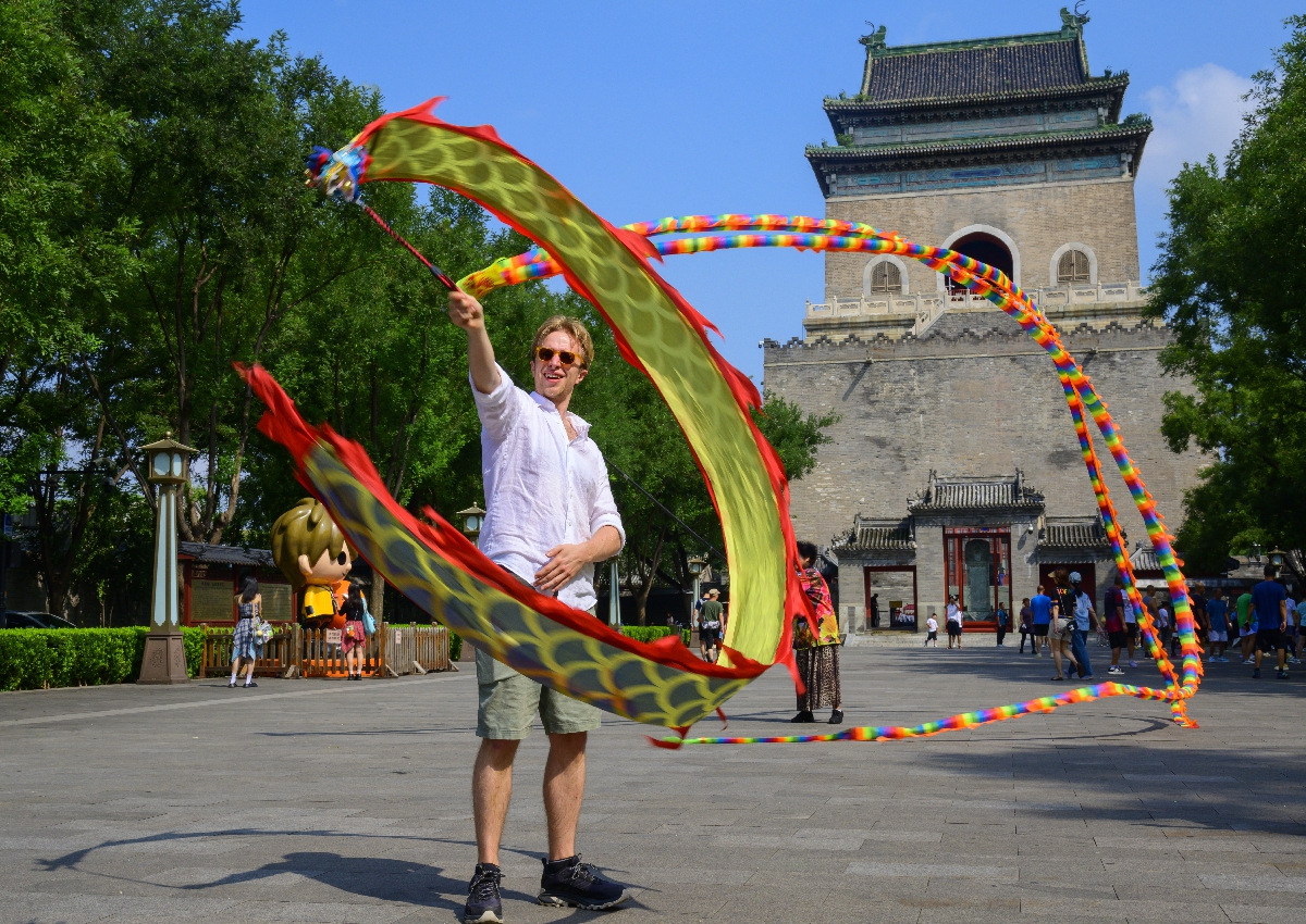 A foreign tourist tries ribbon dragon dancing in front of the Bell Tower, a landmark on the Beijing Central Axis. Photo: VCG