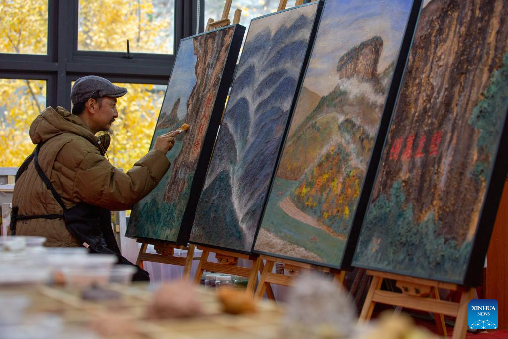An artist works on a piece of rock pigment painting in Wuyishan City, southeast China's Fujian Province, Dec. 5, 2025. Wuyishan boasts a wide range of colorful rock and soil, which serve as a natural palette for painting, giving rise to the distinctive Wuyi rock pigment art. Integrating modern artistic elements and techniques into tradition, Wuyi rock pigment painting is gradually becoming a unique cultural feature of Wuyishan. (Photo by Chen Ying/Xinhua)