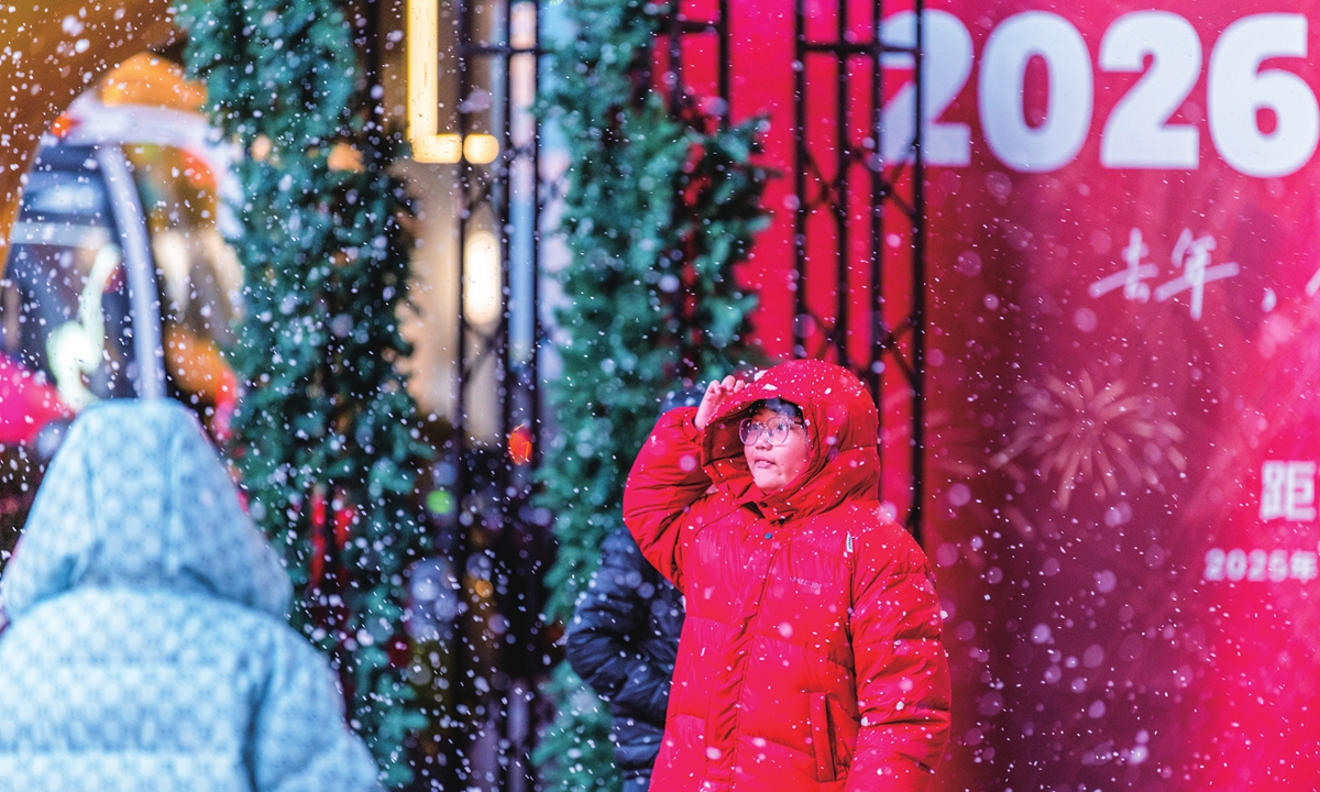 People enjoy the festive atmosphere created by artificial snow nearby the countdown clock for the 2026 New Year in Jinhua, East China's Zhejiang Province on December 21, 2025.
