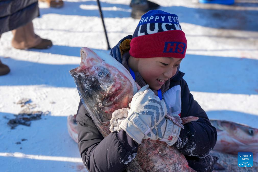 A child poses for a photo with a newly-caught fish during a Nadam fair in Mongolian Autonomous County of Dorbod, Daqing City, northeast China's Heilongjiang Province, Dec. 27, 2025. An ice and snow Nadam fair featuring winter fishing kicked off here on Saturday. The integrated development fishery, and cultural and tourism industry in Dorbod has not only boosted tourism market, but also increased the income of local fishermen. (Xinhua/Wang Song)