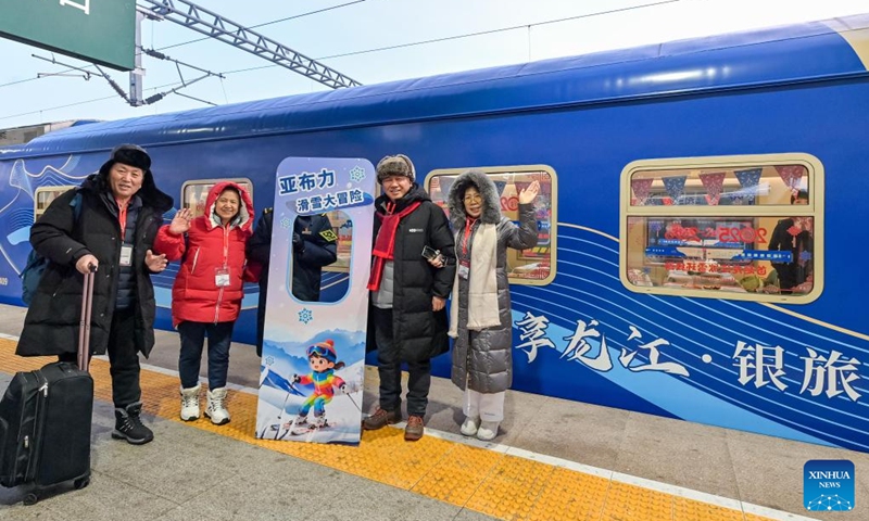 Tourists pose for photos with a tourism train at Harbin East Railway Station in Harbin, northeast China's Heilongjiang Province, Dec. 28, 2025. Train Y999/998, an ice-and-snow themed tourism loop train, started a six-day trip on Sunday. (Photo by Yuan Yong/Xinhua)