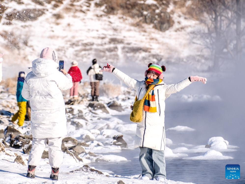 A tourist poses for a photo by the Halha River in the city of Arxan of Hinggan League, north China's Inner Mongolia Autonomous Region, Jan. 1, 2026. Despite Arxan's frigid winter cold, this geothermally-affected section of the Halha River never freezes, which attracts great amount of tourists in winter. (Xinhua/Ma Jinrui)