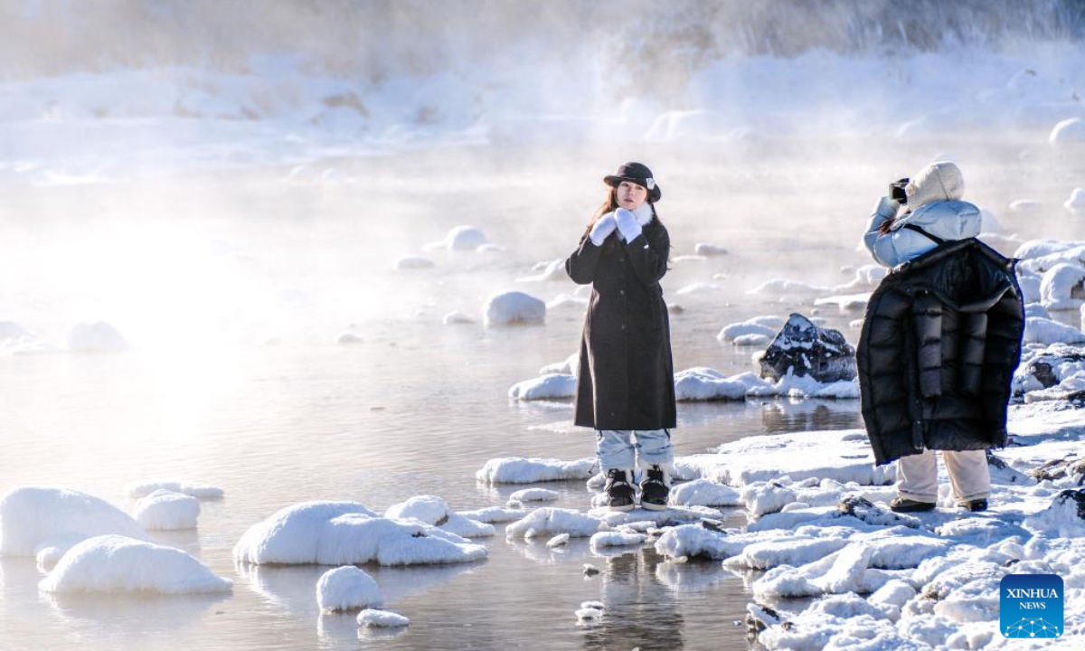 A tourist poses for a photo by the Halha River in the city of Arxan of Hinggan League, north China's Inner Mongolia Autonomous Region, Jan. 1, 2026. Despite Arxan's frigid winter cold, this geothermally-affected section of the Halha River never freezes, which attracts great amount of tourists in winter. (Xinhua/Ma Jinrui)