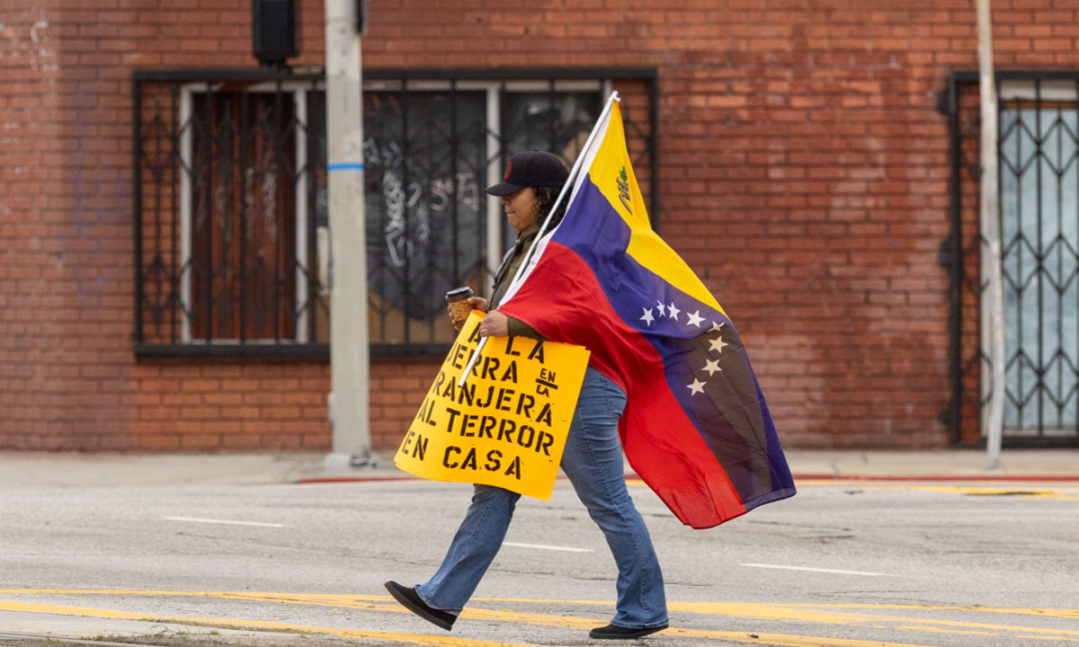 A member of Union del Barrio walks with a Venezuelan flag and a sign in opposition of American intervention on Venezuela prior to a Union del Barrio US out of Venezuela press conference on Saturday, Jan. 3, 2026 in Los Angeles, CA. Photo: VCG