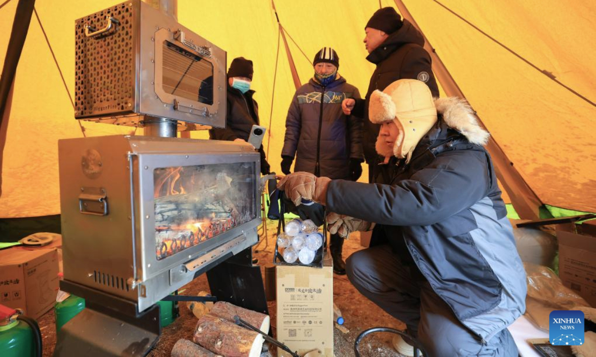 Camping enthusiasts make a fire inside a tent during a camping festival in Qiqihar City, northeast China's Heilongjiang Province, on Jan. 12, 2026. The week-long camping festival opened here on Monday, where camping enthusiasts and tourists across China are allowed to experience the unique charm of camping and local folk customs in frigid chilliness. (Photo by Xu Shuai/Xinhua)
