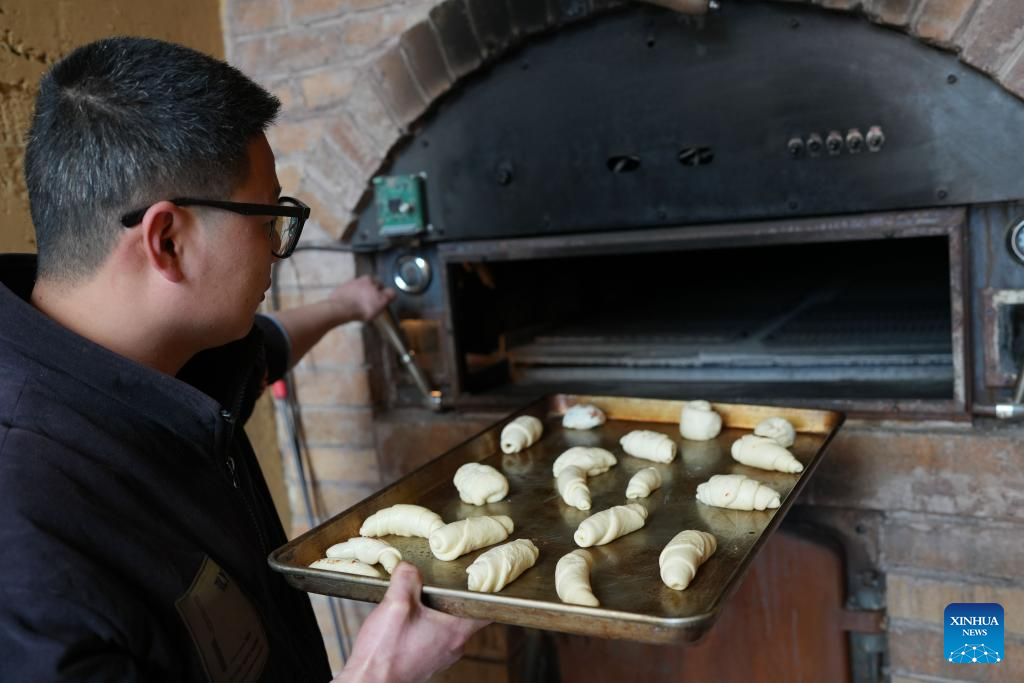 A baker sends bread dough into an oven in Lulikeng Village of Changshan County, east China's Zhejiang Province, Jan. 14, 2026. Lulikeng Village has renovated its abandoned lime kilns into rural tourism facilities in recent years, turning the village into a destination for tourists from surrounding areas. Since 2024, various business sectors in the village have enabled over 150 villagers to find jobs right at their doorstep, and increased the village's income by more than 6 million yuan (about 0.86 million U.S. dollars). (Xinhua/Weng Xinyang)
