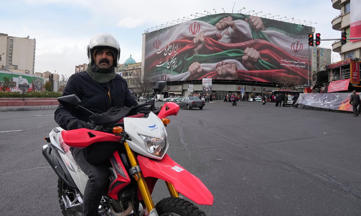 A man drives his motorbike past a huge banner showing hands firmly holding Iranian flags as a sign of patriotism, as one of them flashes the victory sign, in Tehran, Iran, Wednesday, Jan. 14, 2026. Photo: VCG