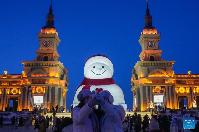 Tourists take selfie in front of the iconic giant snowman at the Qunli music park in Harbin, northeast China's Heilongjiang Province, Jan. 10, 2026. Standing 19 meters tall, measuring 14 meters in length and 11 meters in width, the snowman was dug and carved out of over 3,500 cubic meters of snow, with tourists swarming to take pictures of its classic red scarf and round face. (Xinhua/Wang Jianwei)