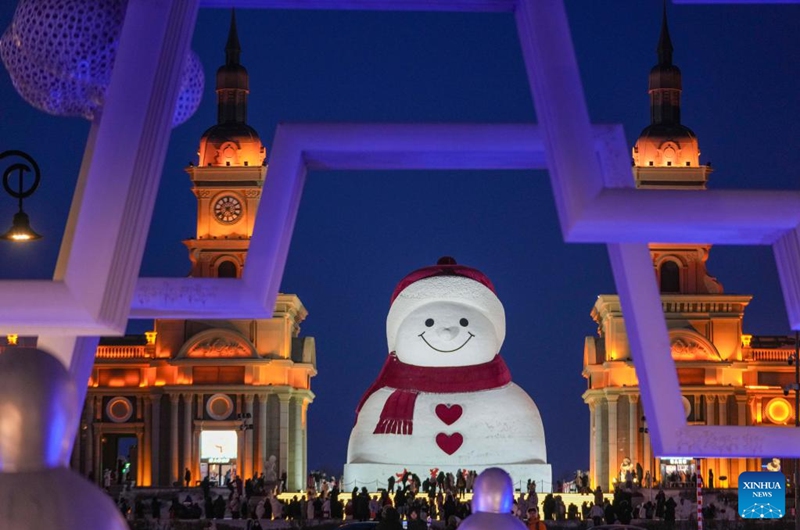 Tourists take photos of the iconic giant snowman at the Qunli music park in Harbin, northeast China's Heilongjiang Province, Jan. 10, 2026. Standing 19 meters tall, measuring 14 meters in length and 11 meters in width, the snowman was dug and carved out of over 3,500 cubic meters of snow, with tourists swarming to take pictures of its classic red scarf and round face. (Xinhua/Wang Jianwei)
