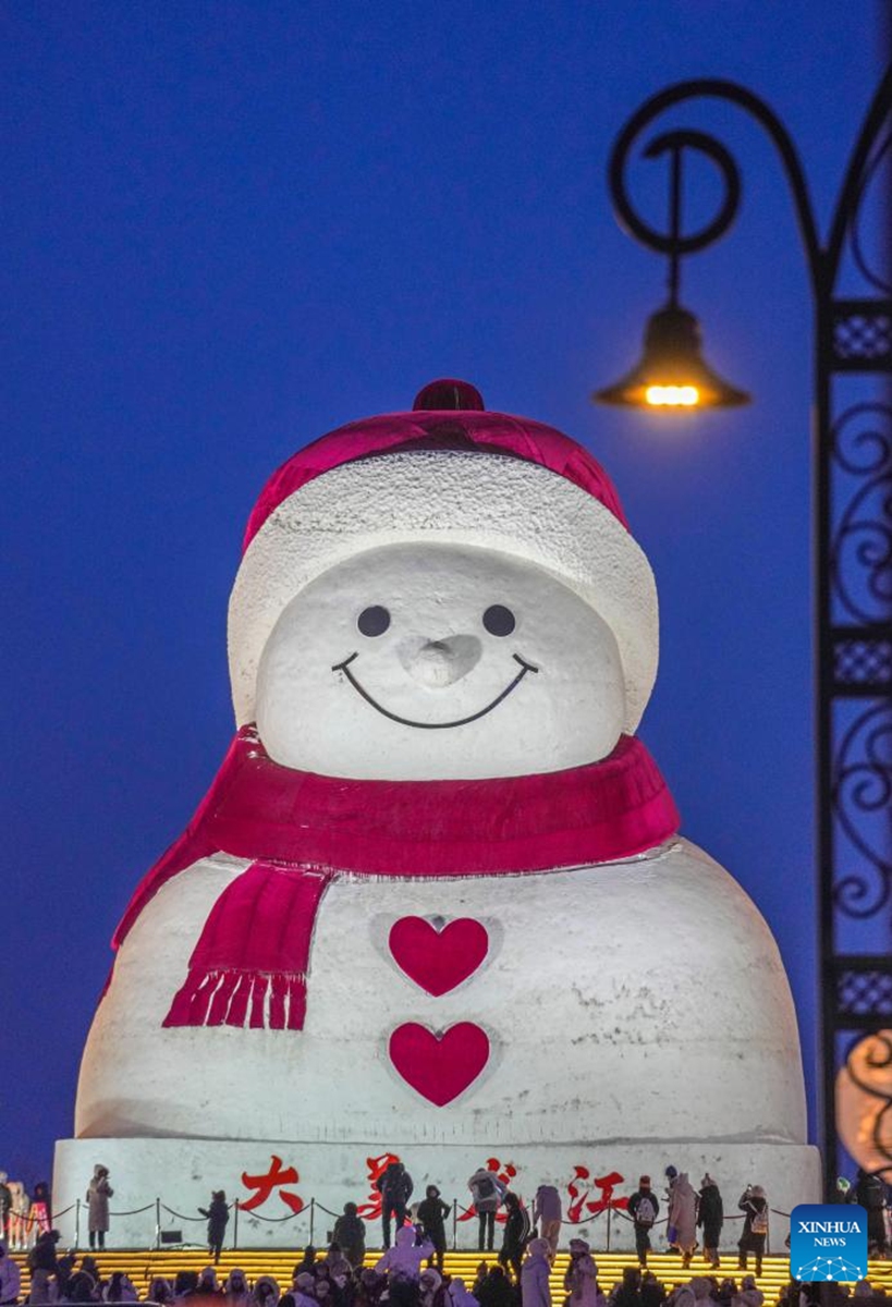 Tourists take photos of the iconic giant snowman at the Qunli music park in Harbin, northeast China's Heilongjiang Province, Jan. 10, 2026. Standing 19 meters tall, measuring 14 meters in length and 11 meters in width, the snowman was dug and carved out of over 3,500 cubic meters of snow, with tourists swarming to take pictures of its classic red scarf and round face. (Xinhua/Wang Jianwei)