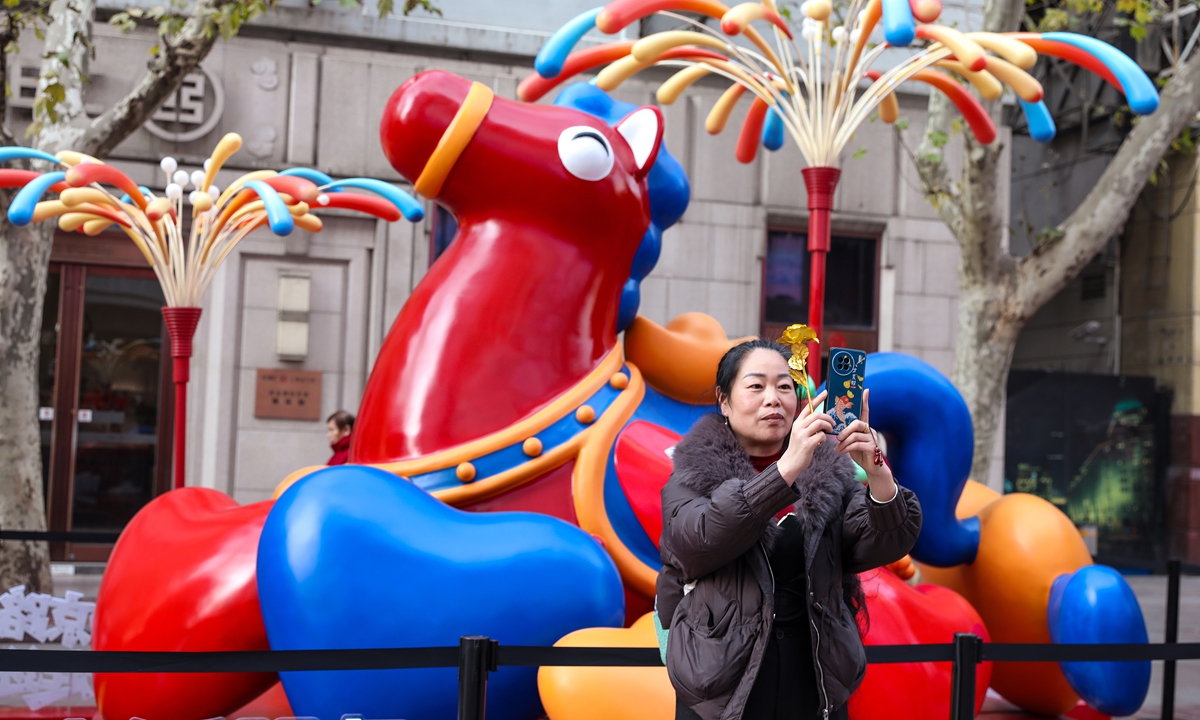 A woman takes a selfie in front of a horse sculpture with a golden ingot on its back in Shanghai on January 13, 2026. To celebrate the upcoming Year of the Horse, the sculpture is named Mashang Youqian, meaning both 