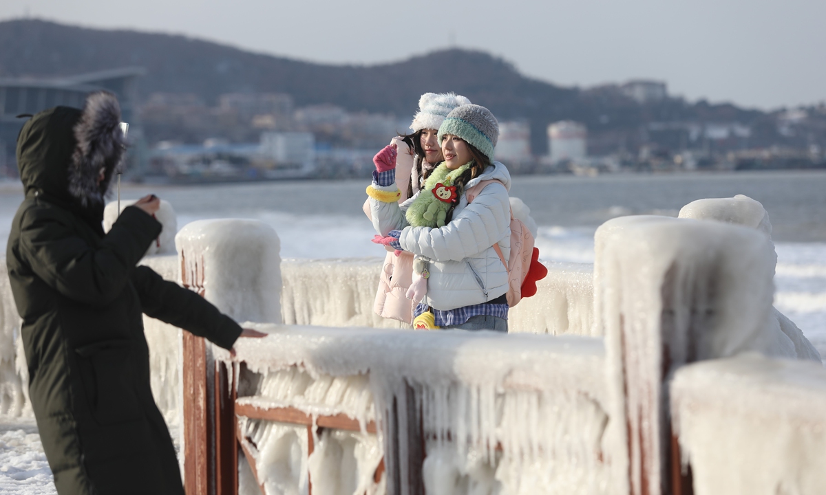 Tourists take photos on the beach in Weihai, East China's Shandong Province on January 21, 2026. Affected by a cold wave, the trestle bridge railings are covered with icicles, creating a scene reminiscent of the 