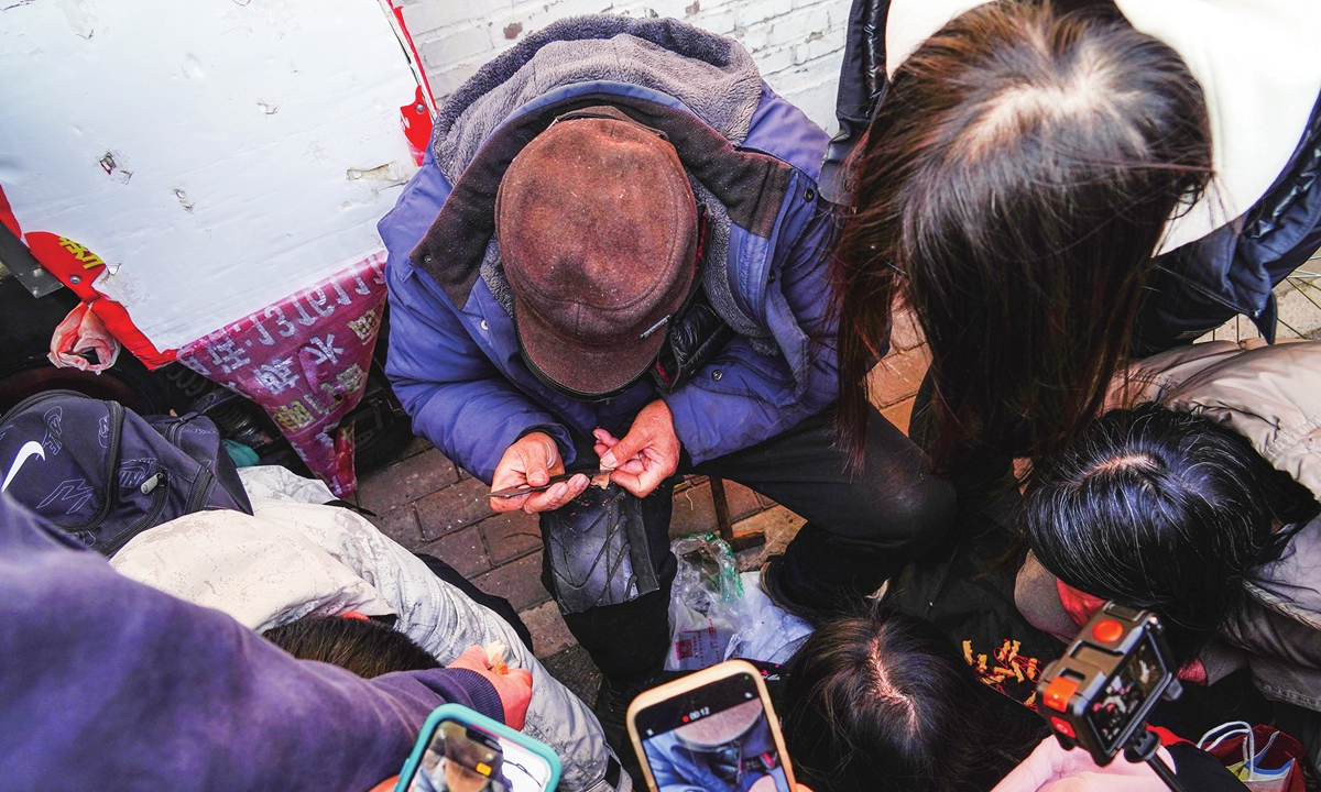 People watch Hu Maoying, known as Shichahai Grandpa, carve wood figurines in Beijing on January 14, 2026. Photo: VCG 