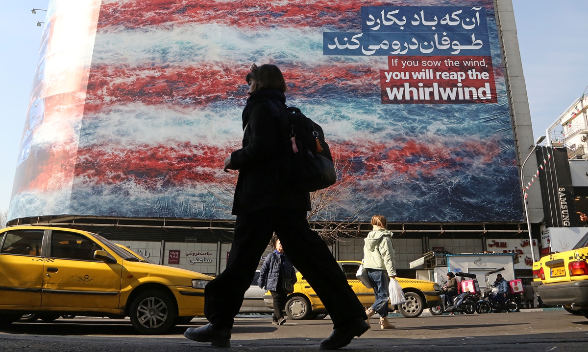 People walk past an anti-American wall poster that reads 'If you sow the wind, you will reap the whirlwind.' following a possible US intervention against Iran on January 28, 2026 in Tehran, Iran. Photo: VCG