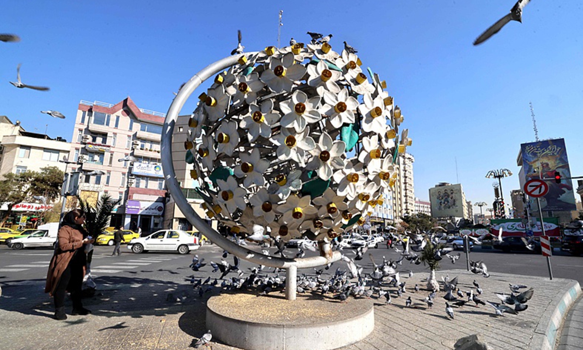 An Iranian woman walks past pigeons gathered at the foot of a sculpture in the Iranian capital Tehran on January 31, 2026, ahead of the 47th anniversary of the 1979 Islamic Revolution.