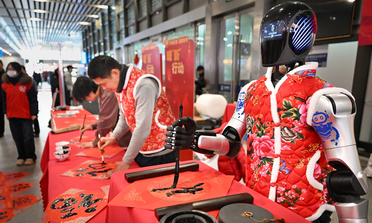 An embodied intelligent robot and calligraphers jointly write the character Fu, which means fortune or blessing, at a rail station in Kunshan, East China's Jiangsu Province on February 2, 2026. The day marks the first day of the Spring Festival travel rush, and the event offers New Year blessings to homebound travelers with a blend of technological innovation and cultural warmth. Photo: VCG