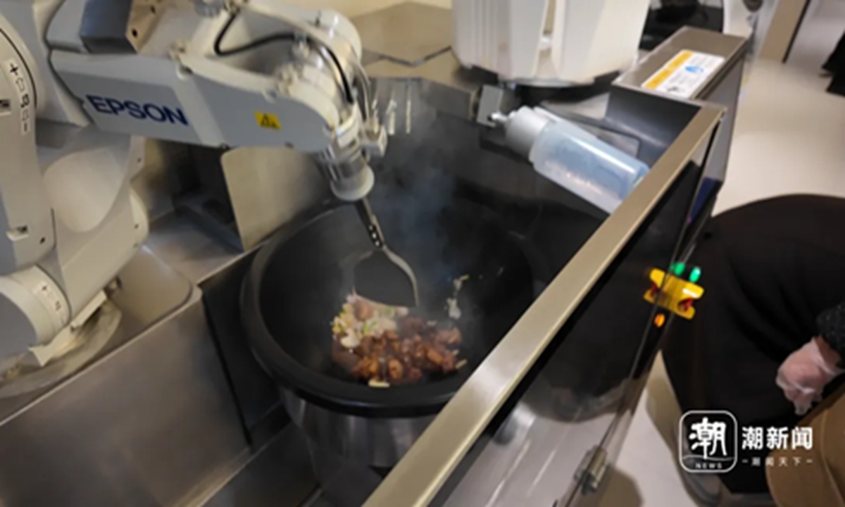 A robot cooking Three-Cup Chicken begins working as the oil heats up, tossing chicken pieces with sauce in the pan in a steady rhythm. Photo: Screenshot from the website