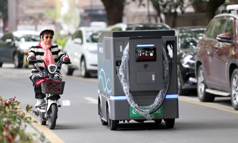 A person rides beside a mobile energy storage charging robot in an old residential community in Hangzhou, East China's Zhejiang Province, on February 10, 2026. The robot, powered by artificial intelligence, can provide on-demand doorstep charging service for three or four electric vehicles per session, taking only 30 to 40 minutes per vehicle. Photo: VCG