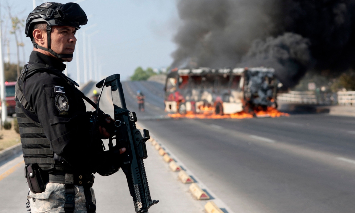 A member of the Prosecutor's Office stands guard after a bus was set on fire by organized crime groups in Zapopan, state of Jalisco, Mexico, on February 22, 2026. The Mexican government said it killed the nation's most wanted cartel boss on Sunday, setting off a wave of violence as cartel members sought revenge. Photo: VCG