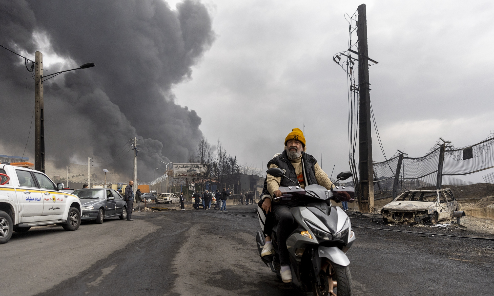 People ride on a motorbike as smoke billows after overnight airstrikes on oil depots on March 8, 2026 in Tehran, Iran. The US and Israel continued their joint attack on Iran while Iran retaliated by firing waves of missiles and drones at Israel, and US bases. Photo: VCG