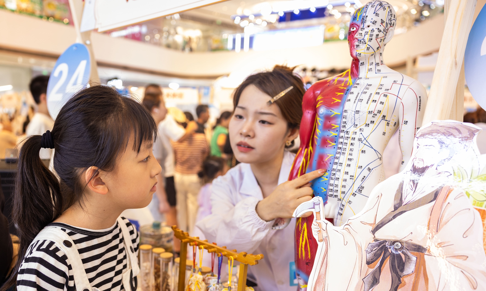 A therapist explains the meridians and acupoints of the human body to a child at a TCM night market in Taizhou, East China's Jiangsu Province, on July 25, 2025. Photo: VCG